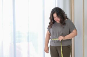 A Síndrome de Cushing é uma patologia que ocorre a partir de um distúrbio na produção de cortisol. Essa doença, que atinge mais as mulheres e traz sintomas muito específicos, exige tratamento porque pode evoluir para problemas graves de saúde. Se quer entender melhor o que é a Síndrome de Cushing, seus sinais e sintomas, leia o texto até o final. O que é Síndrome de Cushing? Quando as pessoas têm excesso do hormônio cortisol no organismo, seja por uma produção endógena ou pelo uso de medicamentos, elas podem desenvolver uma patologia conhecida como hiperadrenocorticismo ou Síndrome de Cushing. Produzido pelas glândulas suprarrenais, que ficam no topo dos rins, o cortisol é conhecido como o hormônio do estresse, e regula diversas funções do organismo, como a glicose no sangue, a pressão arterial, reduz a inflamação no corpo e também transforma o alimento ingerido em energia, ou seja, em condições normais é essencial para o metabolismo. Geralmente, a síndrome afeta 3 vezes mais as mulheres do que homens, e costuma surgir em pessoas entre 30 e 50 anos. Em casos mais raros, pode atingir crianças, que podem ter o crescimento prejudicado. Causas da Síndrome Entre as principais causas para o surgimento da Síndrome de Cushing em uma pessoa, está o uso prolongado de corticoides orais, em altas doses e por longo tempo. Esses medicamentos podem ser necessários no tratamento de lúpus, asma, artrite reumatoide e outras doenças inflamatórias. O uso de corticoides injetáveis para tratar dores nas costas, nas articulações e bursite também surgem como causas da doença. A produção excessiva de cortisol de forma endógena é mais rara, mas pode ser provocada por tumores nas glândulas suprarrenais, na glândula pituitária do cérebro, tumor secretor de ACTH (hormônio adrenocorticotrópico, que pode ser benigno ou maligno), por herança genética, desnutrição, treinos intensos, alcoolismo e altos níveis de estresse. Tumores que levam à Síndrome de Cushing Glândula pituitária: 8 de cada 10 casos de Síndrome de Cushing são resultado desses tumores. Ocorre quando o cortisol é produzido em excesso pela glândula pituitária, que recebe estímulo da superprodução de ACTH pela hipófise. Quando é fruto da glândula pituitária passa a se chamar doença de Cushing e também afeta mais as mulheres. Os adenomas hipofisários não costumam ser malignos. Adrenal: esse tipo de tumor costuma ser benigno, porém, pode ocorrer também uma malignidade. Tumor secretor de ACTH: em boa parte das vezes, esses tumores ocorrem nos pulmões, tireoide, pâncreas e glândula timo. Podem ser cancerosos. Síndrome de Cushing: sintomas Os sintomas de Síndrome de Cushing podem começar gradualmente ou de forma repentina e, inclusive, podem ser perceptíveis na própria silhueta do paciente. Os sinais mais típicos de quem tem a doença são: Rosto arredondado, inchado e avermelhado; Ganho de peso com acúmulo de gordura na nuca (corcunda de búfalo), ombros e abdômen, embora os braços continuem mais finos; Estrias na pele. As mulheres que sofrem com a patologia também podem apresentar pelos faciais e corporais no rosto, pescoço, peito e coxas, além de irregularidades no ciclo menstrual. Enquanto os homens podem manifestar também disfunção erétil e redução da fertilidade. Porém, para quem tem a Síndrome de Cushing, os sinais e sintomas também podem ser fraqueza nas coxas e braços, fadiga, acne, pele que machuca facilmente, mudanças de humor, dores de cabeça, escurecimento da pele, depressão e redução da libido, em ambos os sexos. Leia também sobre: Bexiga hiperativa Dor na bexiga – Diagnóstico de Síndrome de Cushing Diagnosticar a doença nem sempre é tão fácil, porque seus sinais e sintomas se confundem com os de muitas outras patologias, por isso, a consulta pode começar por um diagnóstico de exclusão. Além disso, o médico irá investigar as queixas dos pacientes, as características físicas que apontam para a doença. Caso o paciente não esteja tomando corticoides, o médico também pode pedir exames de laboratório, como de sangue, teste de cortisol urinário livre, hormonais e de saliva, e outros de imagem, que permitam a visualização das glândulas adrenais e pituitária. Além de trazer mais dados que apontam para a patologia, os exames também vão ajudar a descartar ou confirmar outras doenças. Síndrome de cushing: tratamento O tratamento da Síndrome de Cushing é essencial para aliviar os sintomas e evitar complicações, como o surgimento de outras patologias, como infecções frequentes, derrames e ataques cardíacos, perda de massa muscular, osteoporose, que podem levar a muitas fraturas ósseas; perdas de memória, problemas cognitivos, síndrome metabólica, pressão alta, diabetes tipo 2, etc. O tratamento consiste em reduzir os níveis de cortisol no organismo. Caso o paciente já informe ao médico que usa corticoides de forma contínua, o especialista poderá fazer uma revisão em seus medicamentos e reduzir as doses. Porém, nunca reduza as doses sem supervisão médica. Já se a síndrome tiver sido causada por um tumor existem algumas opções, como a cirurgia para remover o tumor. No entanto, para alguns pacientes a cirurgia não é possível, então, o médico pode indicar o uso de uma combinação de medicamentos que reduzam a produção do cortisol no organismo pelas suprarrenais ou glândula pituitária. Conclusão Se você apresenta as características apontadas acima, procure um médico para avaliar sua saúde. É essencial tratar a Síndrome de Cushing para que a patologia não provoque doenças graves para o paciente. Além dos medicamentos, algumas alterações nos hábitos de vida também podem ajudar no tratamento, como a perda de peso, reduzir o sal e o açúcar da dieta, além de evitar o consumo de álcool. Leia também: Incontinência urinária